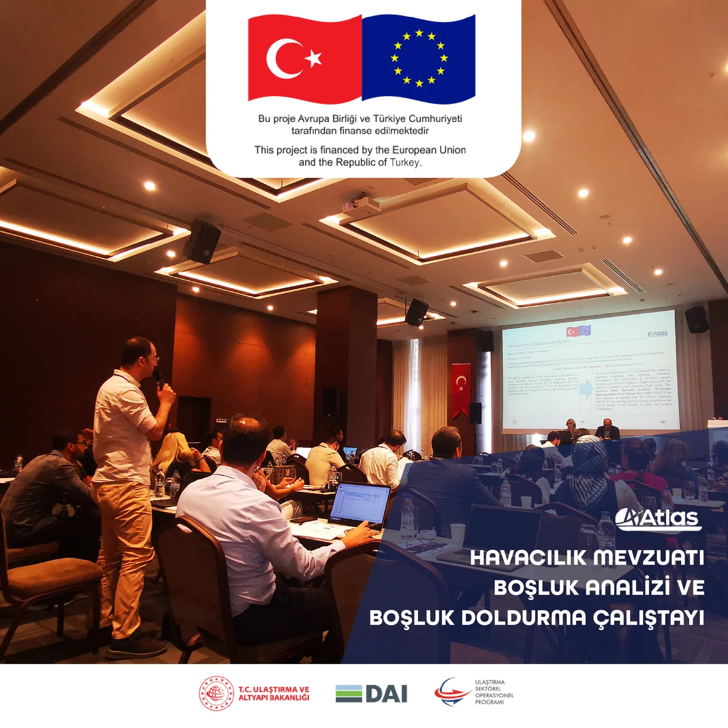 A workshop room photographed from the back, the designed backdrop and projection screen carrying the programme title, the Turkish flag, the European Union emblem and the funding statement.