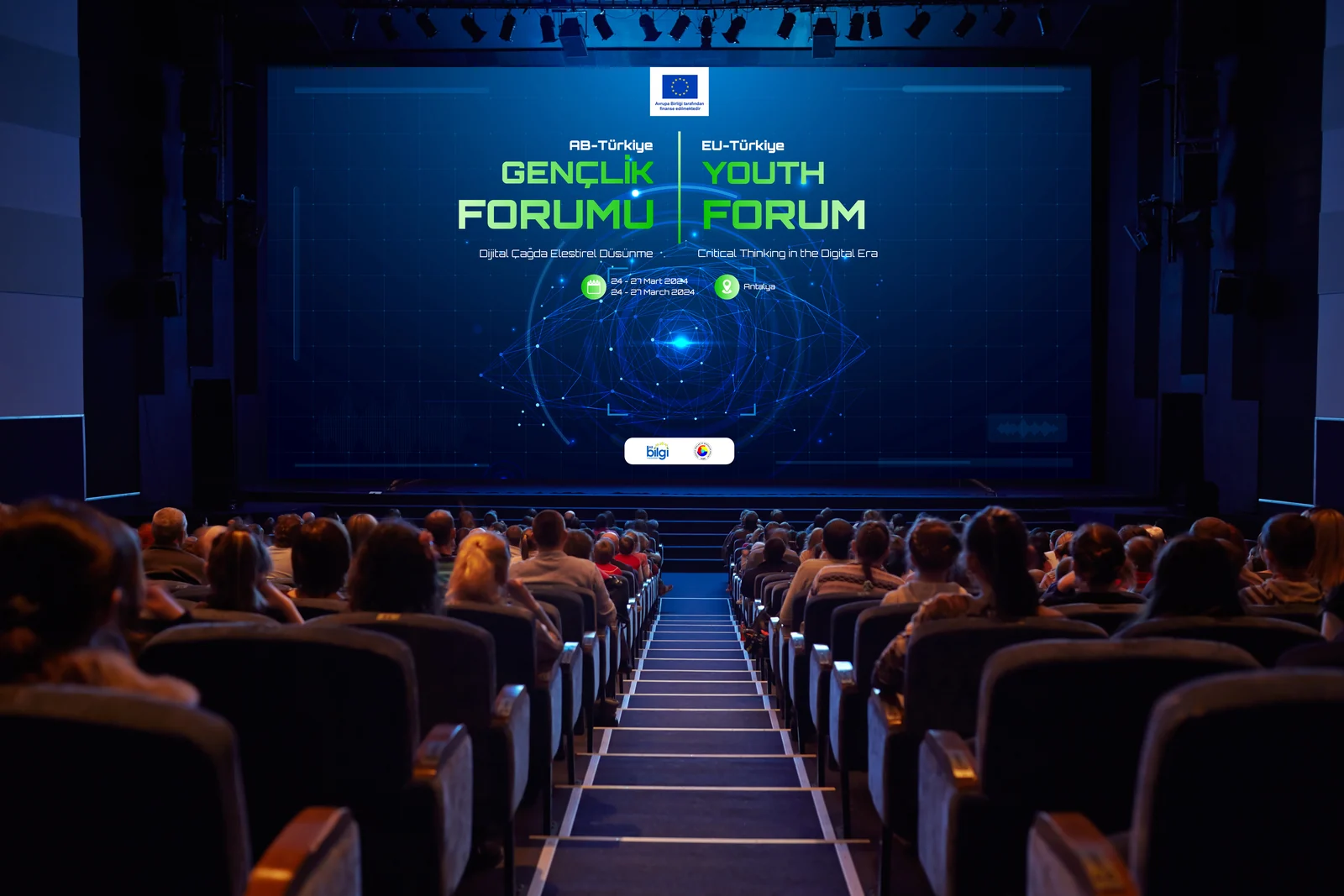 A darkened auditorium facing a wide stage screen that carries the forum identity in Turkish and English, with the audience seated in rows below.