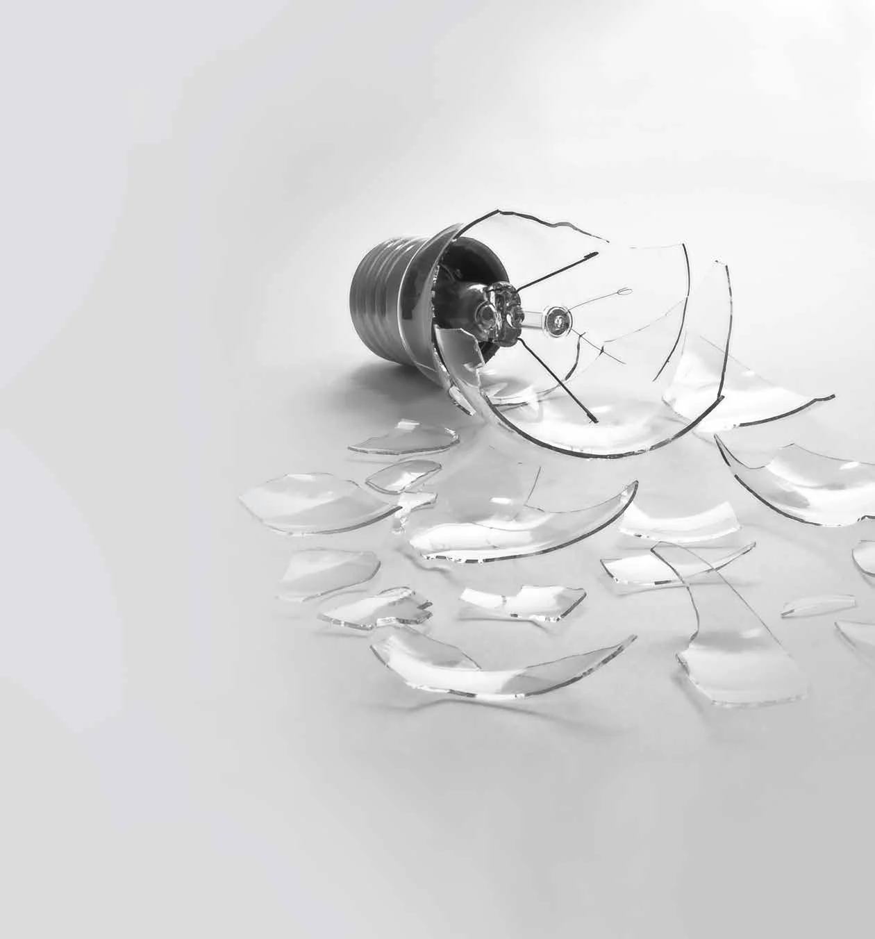 A shattered light bulb photographed on white, its glass fragments spread out.
