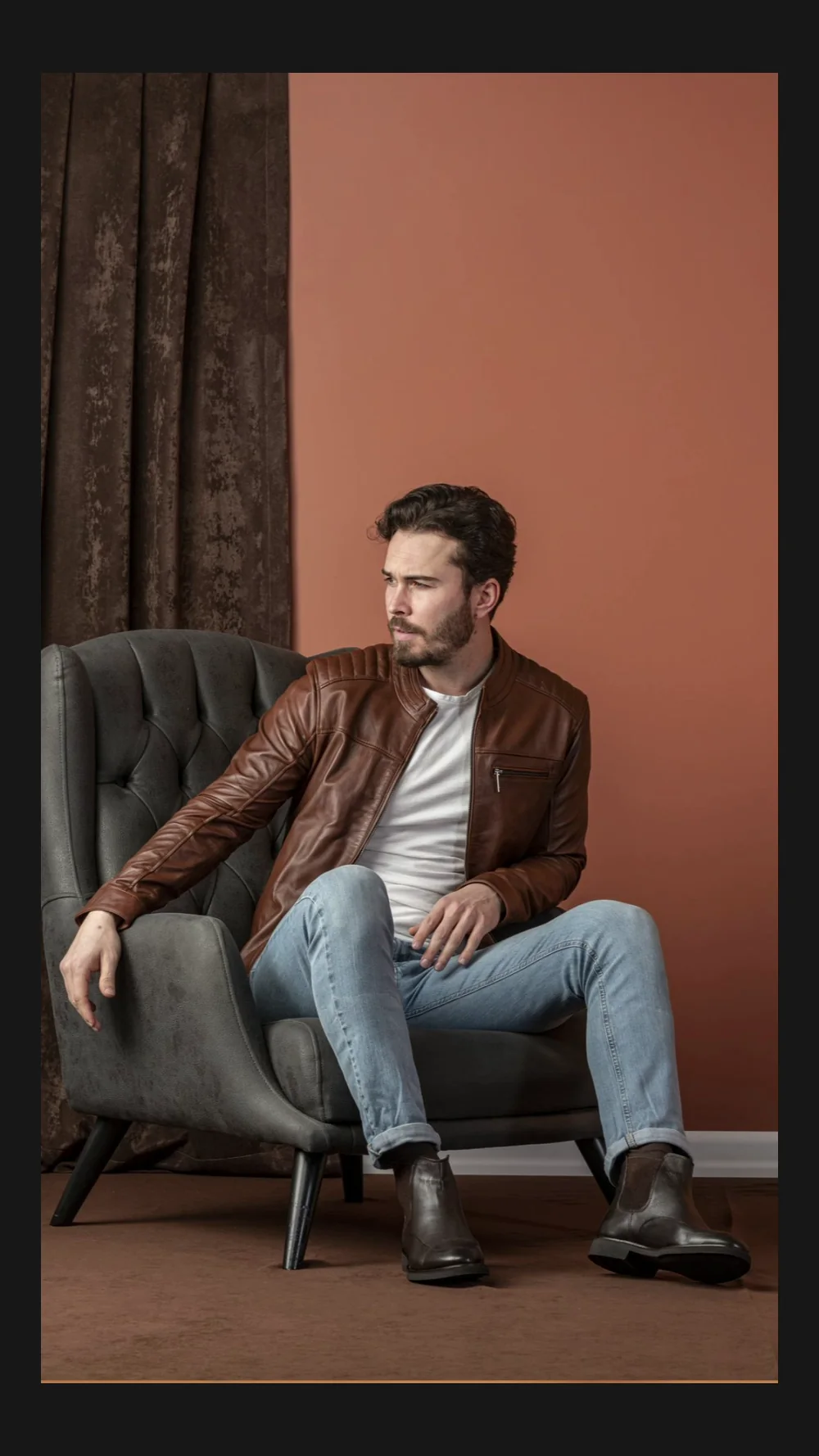 A frame from a category film, a model seated in an armchair against a rust wall.